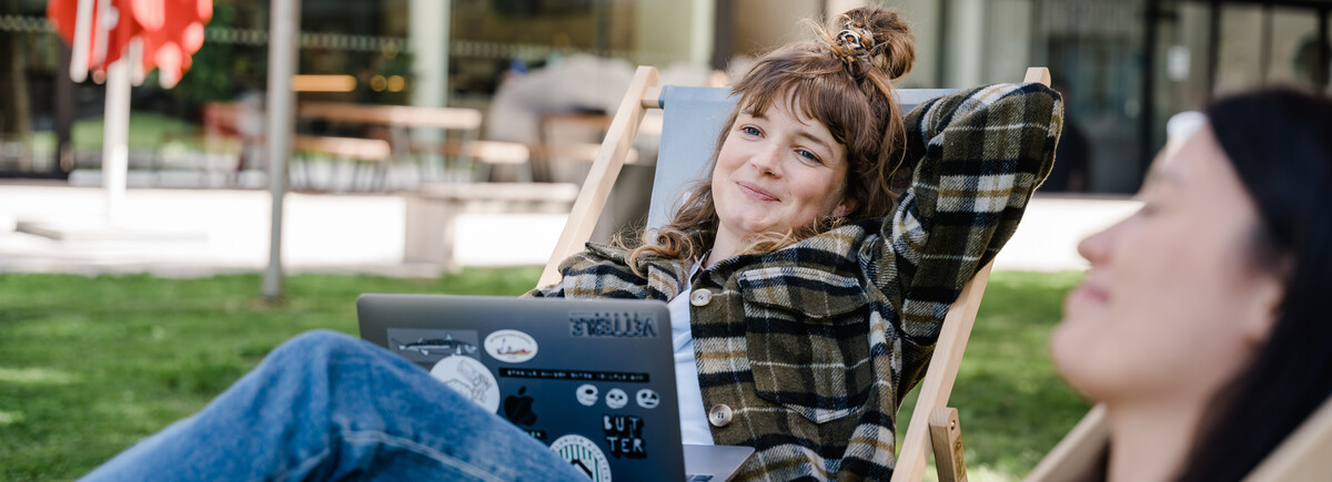 Zwei Studierende der FH Kufstein Tirol arbeiten entspannt im Freien auf Liegestühlen am Campus.