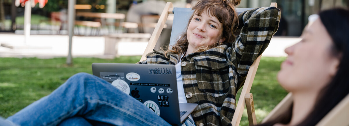 Zwei Studierende der FH Kufstein Tirol arbeiten entspannt im Freien auf Liegestühlen am Campus.