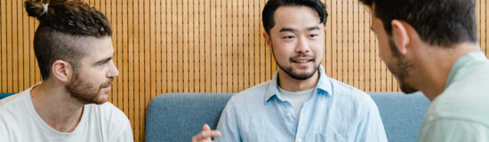 Drei Studierende im Gespräch bei Gruppenarbeit mit Laptop in moderner Sitzecke