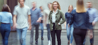 Viele Personen bewegen sich durch die Aula der FH Kufstein Tirol, und im Zentrum des Bildes steht eine Frau und blickt in die Kamera.