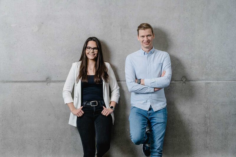 Zwei Studierende der FH Kufstein Tirol vor einer Betonwand – Portrait im modernen Campusstil.
