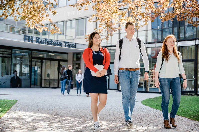 Drei Studierende der FH Kufstein Tirol gehen über den Campus vor dem Hauptgebäude.