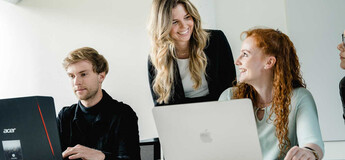 Dozentin im Gespräch mit Studierenden bei gemeinsamer Arbeit am Laptop an der FH Kufstein Tirol.
