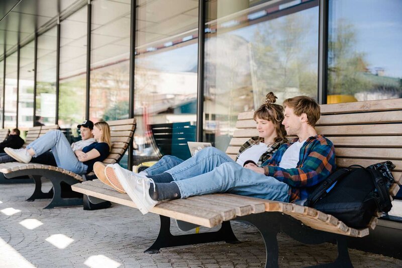 Studierende der FH Kufstein Tirol nutzen die Holzliegen vor dem Hochschulgebäude zum Lernen und Entspannen.