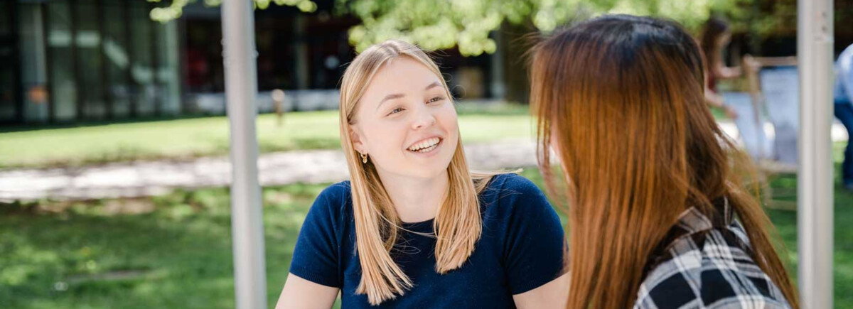 Zwei Studierende der FH Kufstein Tirol im Gespräch auf dem Campusgelände an einem sonnigen Tag.