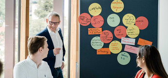 Dozent der FH Kufstein Tirol erläutert Studierenden Seminarinhalte an einer Pinnwand mit Notizen