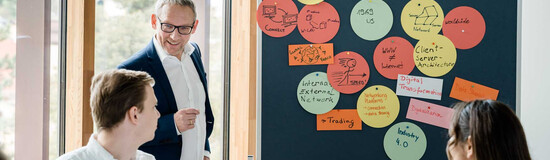 Dozent der FH Kufstein Tirol erläutert Studierenden Seminarinhalte an einer Pinnwand mit Notizen