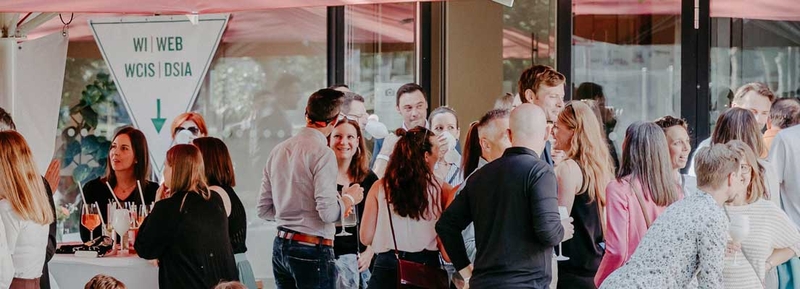 Alumni und Mitarbeiter:innen der FH Kufstein Tirol beim Home Coming 2024 im lebhaften Austausch auf der Campus-Terrasse.