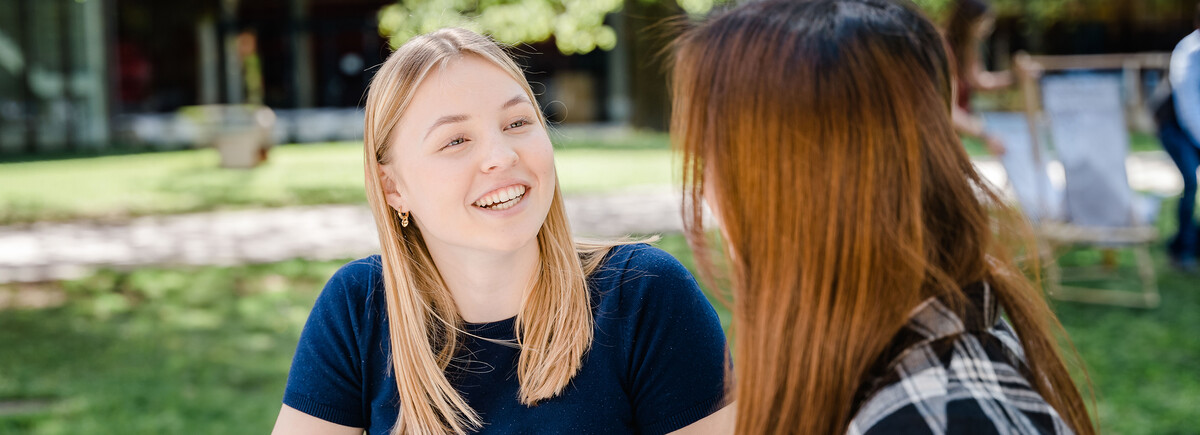 Schulen | © FH Kufstein Tirol Zwei Frauen sitzen im Park der Hochschule und sprechen lächelnd miteinander. | © FH Kufstein Tirol