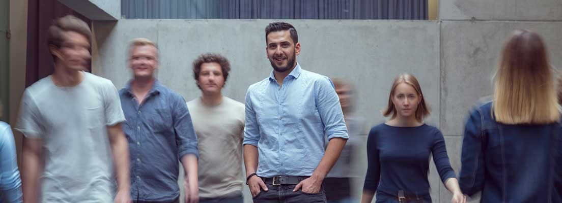 Viele Personen bewegen sich durch die Aula der FH Kufstein Tirol, und im Zentrum des Bildes steht ein Mann und blickt in die Kamera.