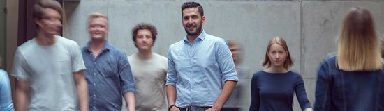 Viele Personen bewegen sich durch die Aula der FH Kufstein Tirol, und im Zentrum des Bildes steht ein Mann und blickt in die Kamera.