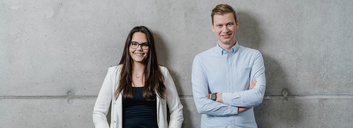 Studienguide_Sektion_2 | © FH Kufstein Tirol Eine Frau und ein Mann stehen zusammen bei einer Wand und lächeln in die Kamera. | © FH Kufstein Tirol