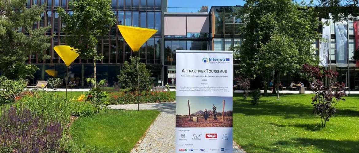 Attraktiver_Tourismus | © FH Kufstein Tirol Im Zentrum ist ein Plakat des Forschungprojekts "Attraktiver Tourismus", welches im Campus Park der Fachhochschule Kufstein Tirol steht. | © FH Kufstein Tirol