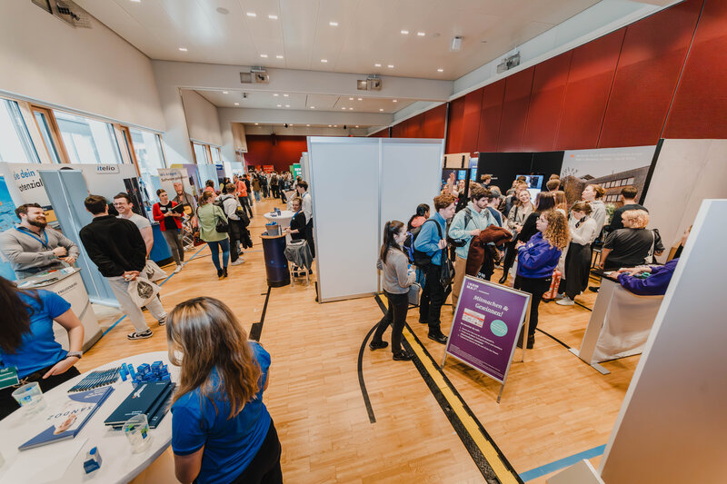 Besucher:innen der Meet & Match 2024 an der FH Kufstein Tirol, fotografiert aus erhöhter Position, während sie sich an den Ständen informieren. | © FH Kufstein Tirol 