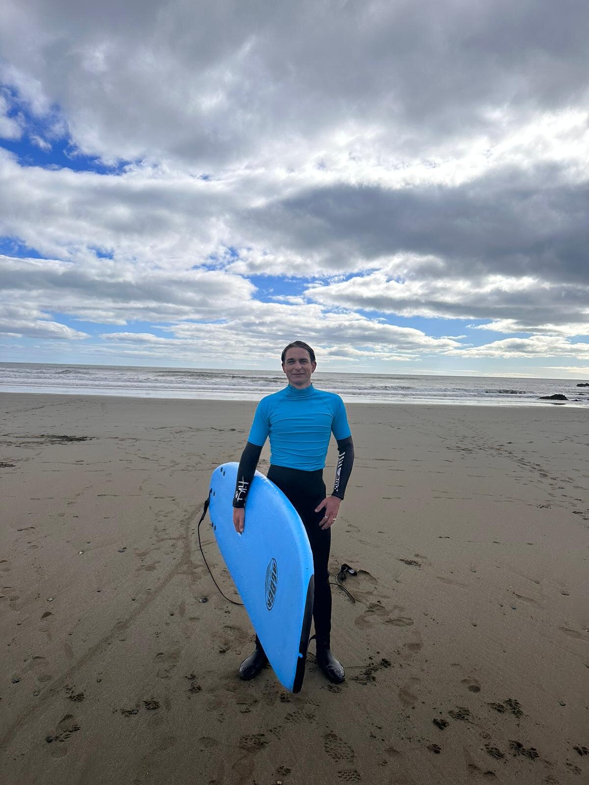 Auslandssemester Irland 2024 | © Andreas Schmieger Ein junger Mann in einem Neoprenanzug und blauem Shirt mit einem Surfboard am Strand. | © Andreas Schmieger