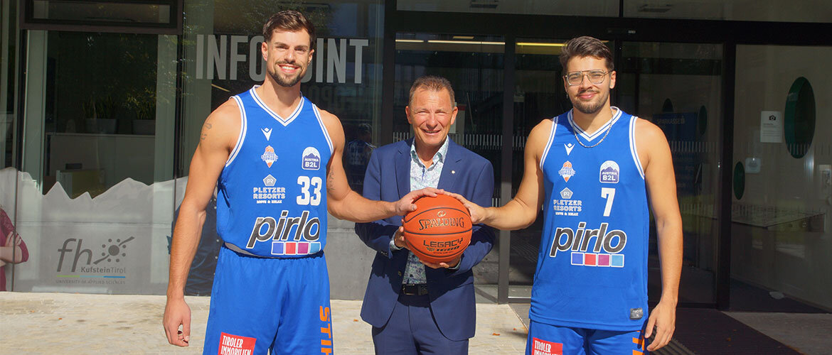 Zwei Basketballspieler und der Geschäftsführer der FH Kufstein Tirol mit einem Ball vor dem Eingang der Fachhochschule.