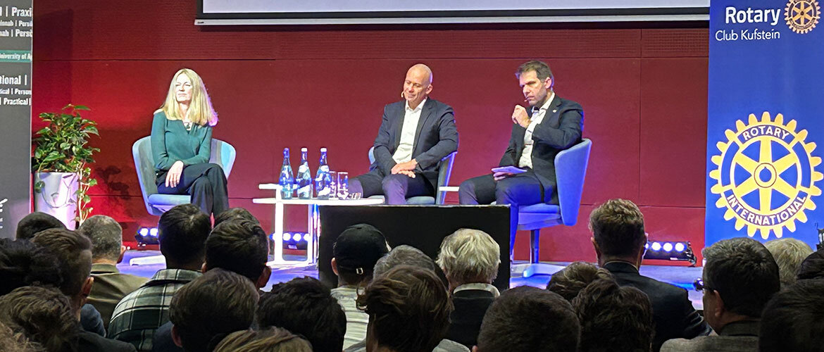 Management Forum – Podiumsdiskussion mit Expert:innen und Rotary Club Kufstein. Drei Expert:innen diskutieren auf einer Bühne im Festsaal der FH Kufstein Tirol beim Management Forum, während das Publikum aufmerksam zuhört. Rechts steht ein Banner des Rotary Clubs Kufstein.