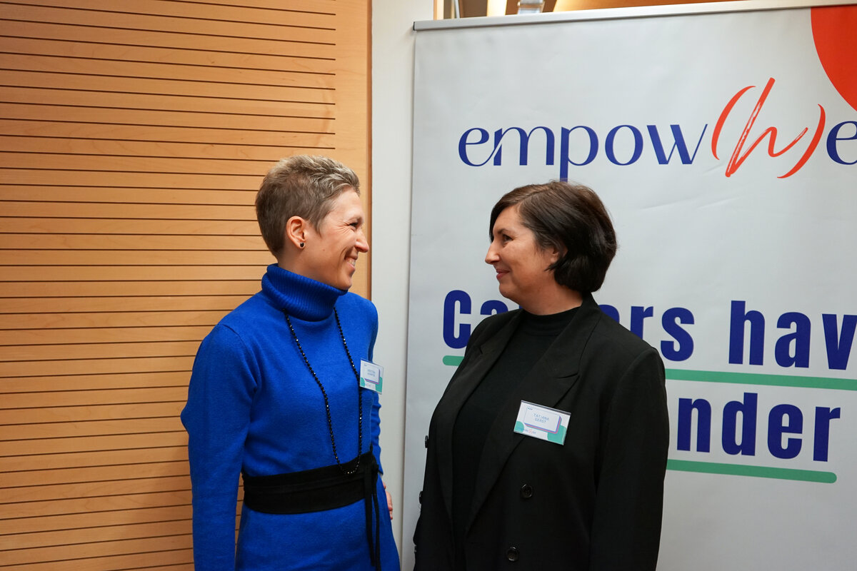 Interview Empow(h)er Porträt | © FH Kufstein Tirol Zwei Frauen stehen vor einem Banner und schauen sich gegenseitig an. | © FH Kufstein Tirol