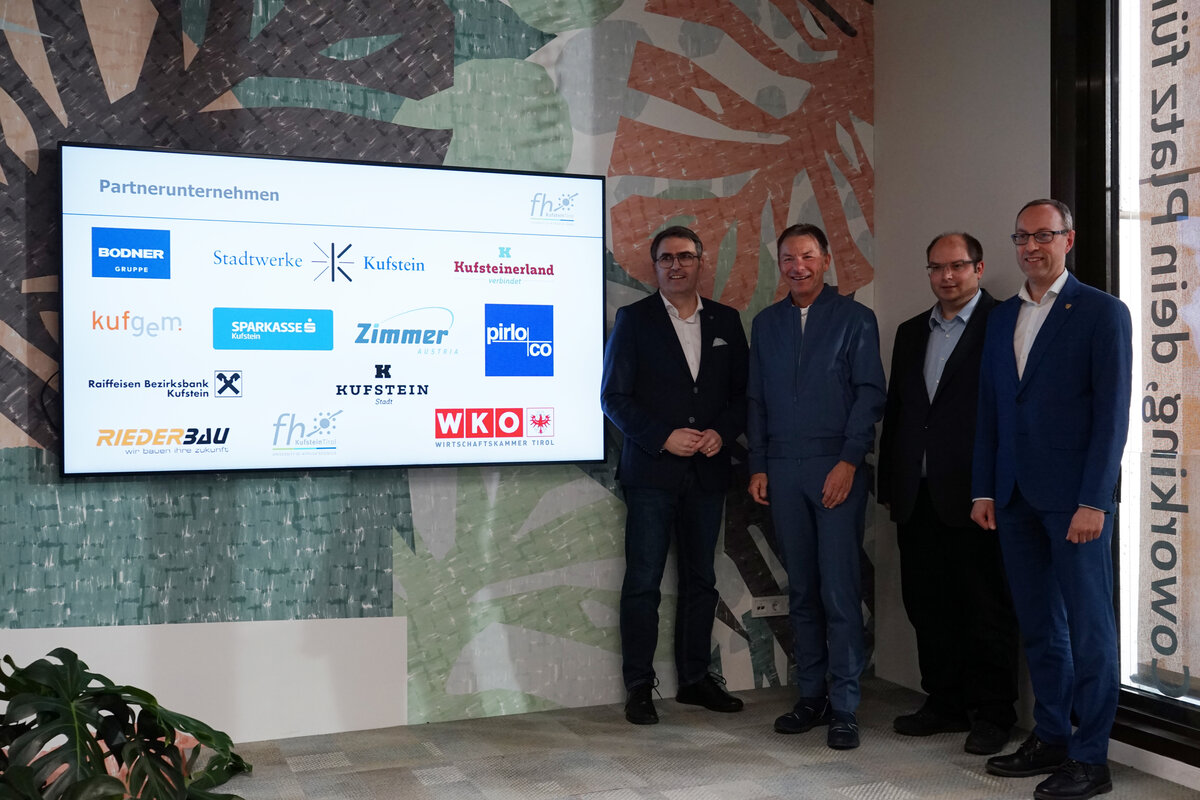 Vier Männer in Anzügen stehen rechts neben einem Bildschirm mit Logos. | © FH Kufstein Tirol
