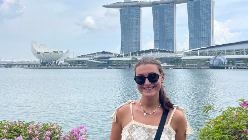 Privat | © Magdalena Bernrieder posiert vor einer modernen Skyline in Malaysia, mit einem ruhigen Gewässer im Hintergrund.
