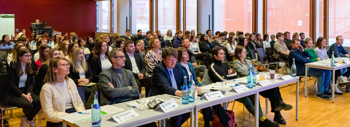 7-Euro-Cash-at-School-Wettbewerb-Publikum-Festsaal-FH-Kufstein-Tirol | © FH Kufstein Tirol Ein Blick ins Publikum des Festsaals der FH Kufstein Tirol: In der ersten Reihe sitzen die Juror:innen des 7€ Cash@School-Wettbewerbs, dahinter die Schüler:innen. | © FH Kufstein Tirol