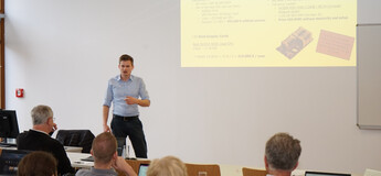 Alexander Schiegl hält einen Vortrag beim Workshop über den Einsatz von KI-Agenten im Marketing an der FH Kufstein Tirol. Die Präsentation im Hintergrund zeigt Berechnungen zu Grafikkartenkosten. | © FH Kufstein Tirol