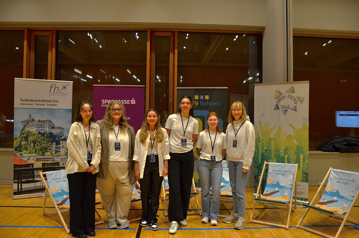projektteam-table-tennis-tournament-fh-kufstein-tirol | © FH Kufstein Tirol Eine Gruppe von sechs jungen Frauen steht in einer Sporthalle vor Bannern der FH Kufstein Tirol, der Sparkasse Kufstein und des Green Event Tirol. Sie tragen Namensschilder und lächeln in die Kamera. | © FH Kufstein Tirol