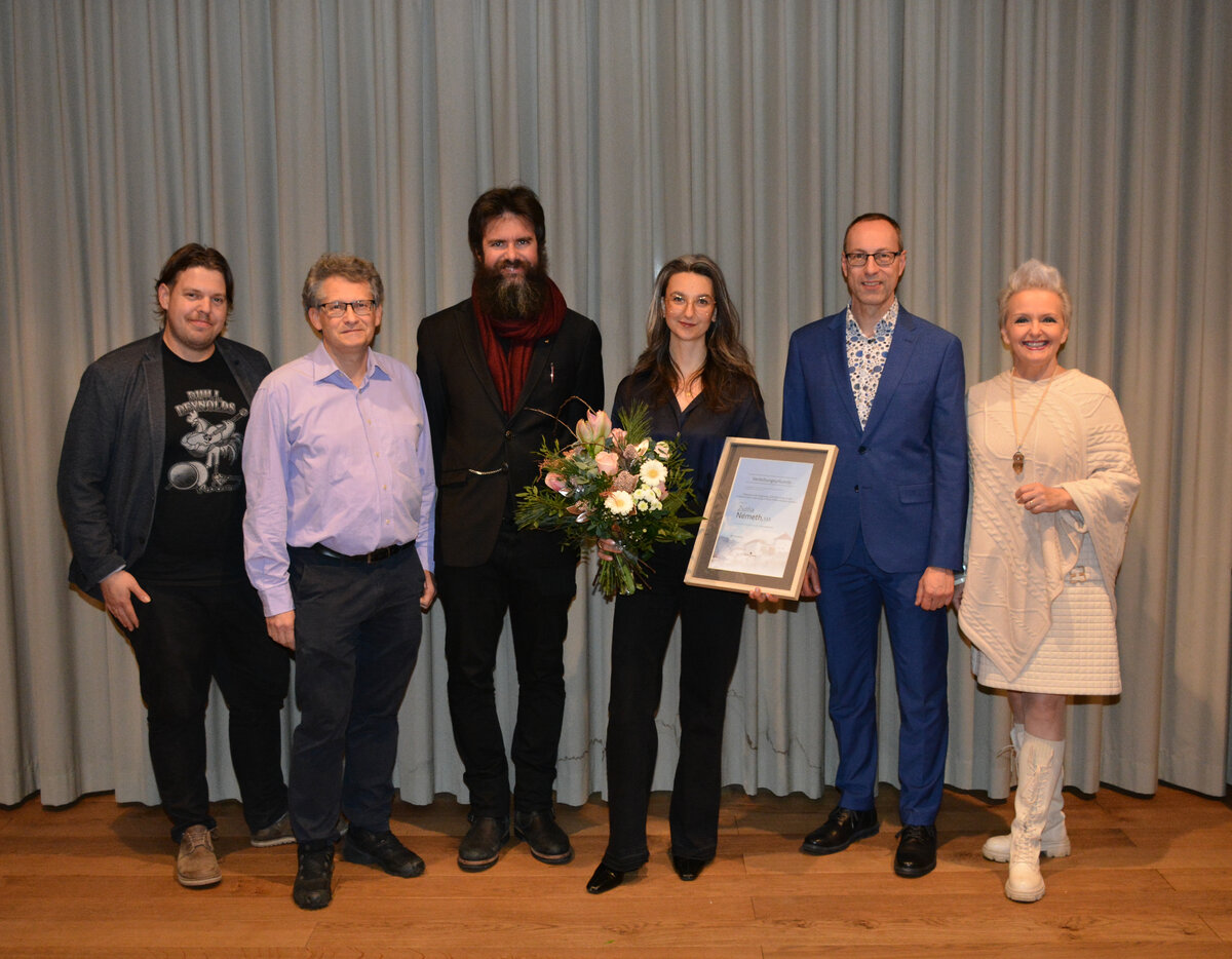 Sechs Personen stehen nebeneinander vor einem grauen Vorhang. In der Mitte hält Preisträgerin Zsófia Németh eine Urkunde und einen Blumenstrauß. Neben ihr stehen Vertreter aus Bildung, Kultur und Stadtpolitik, darunter Harald Stoiber, Reinhold Weichselbraun, Klaus Reitberger, FH-Rektor Mario Döller und Vizebürgermeisterin Brigitta Klein. | © Standortmarketing Kufstein