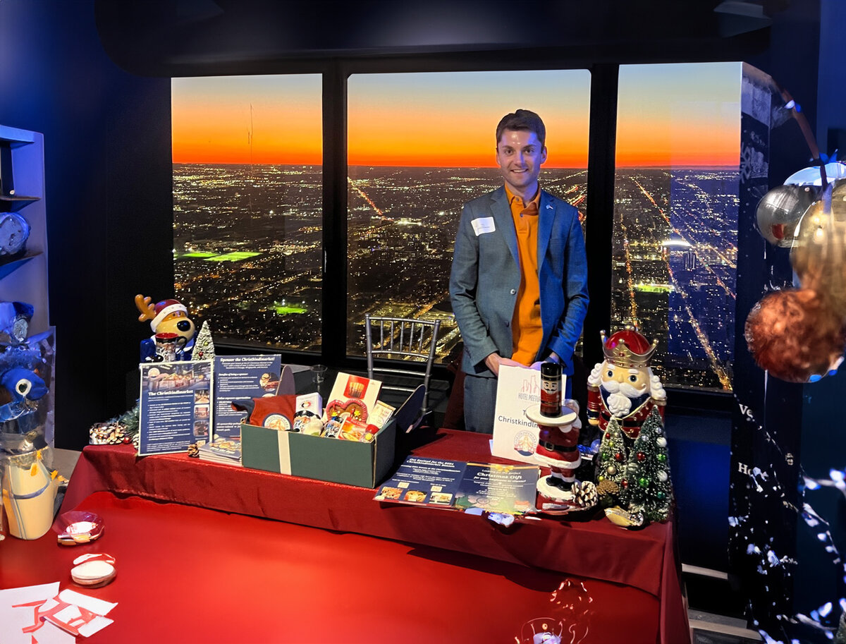 Chicago-Toni-Pötzl | © privat ki-adaptiert Toni Pötzl vor einem Messestand mit Blick auf die Stadt bei Nacht | © privat ki-adaptiert