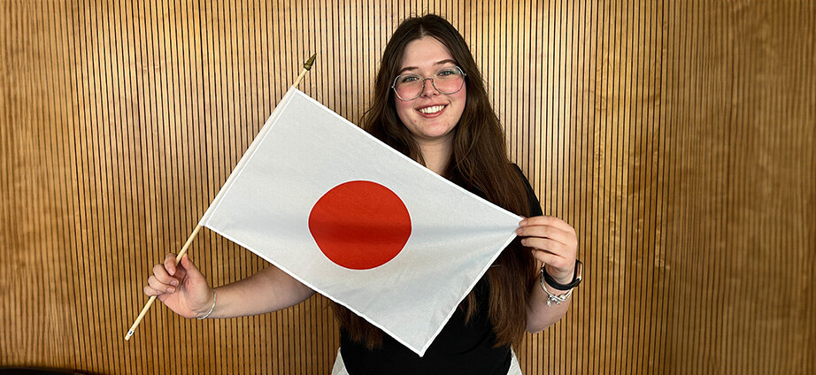 Vorbereitung Auslandssemester Felicia | © FH Kufstein Tirol ki-adaptiert Studentin steht vor einer Holzwand mit einer Japan-Flagge | © FH Kufstein Tirol ki-adaptiert