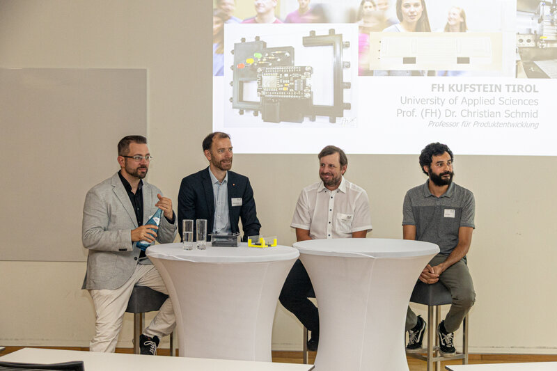 Vier Personen sitzen vor einem Stehtisch, im Hintergrund eine Präsentation. | © FH Kufstein Tirol 