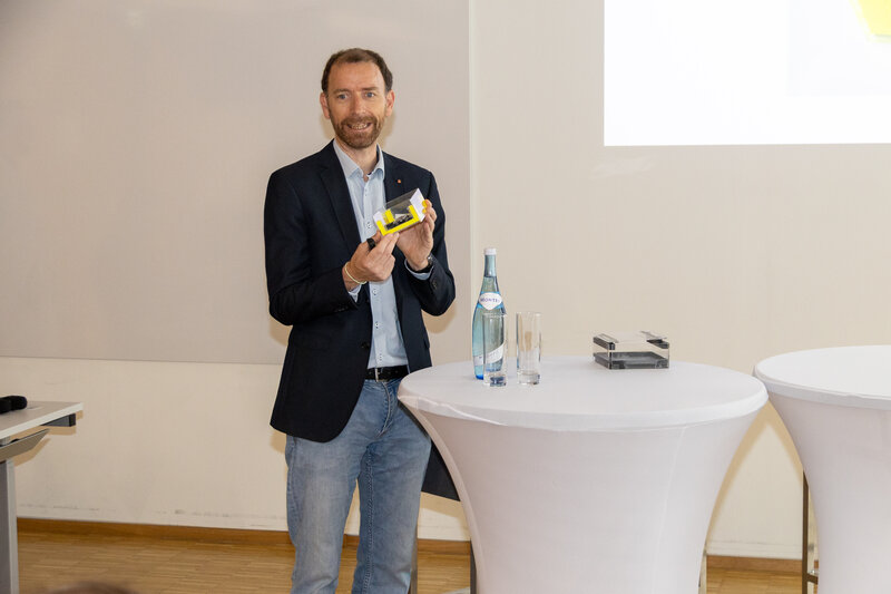 Ein Mann hat einen gelben Zettel in der Hand und steht vor einem Stehtisch. | © FH Kufstein Tirol 