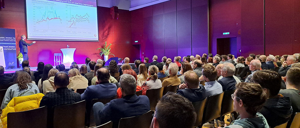 Vortragender zeigt auf eine Präsentationsfolie mit Diagrammen beim Management Forum der FH Kufstein Tirol, während ein vollbesetzter Saal gespannt zuhört.