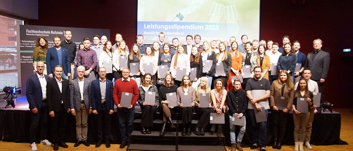 Eine große Gruppe von Studierenden und Dozierenden posiert im Festsaal der FH Kufstein Tirol bei der Verleihung des Leistungsstipendiums 2023. Viele der Studierenden halten ihre Urkunden in den Händen.