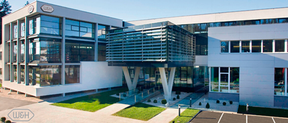 Modernes Firmengebäude der W&H Gruppe mit Glasfassade und vorgelagertem Eingangsbereich.