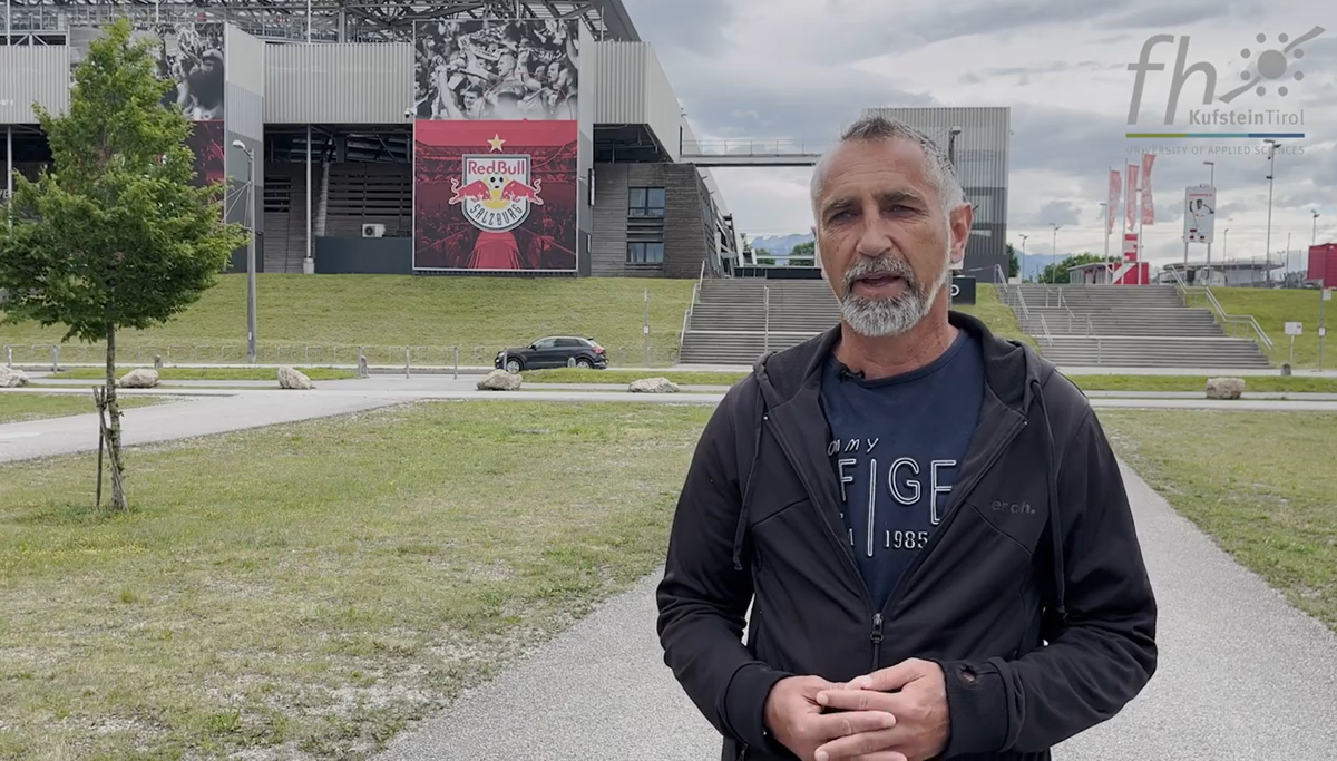 Man in a black hoodie standing infront of the Red Bull Salzburg Stadium.