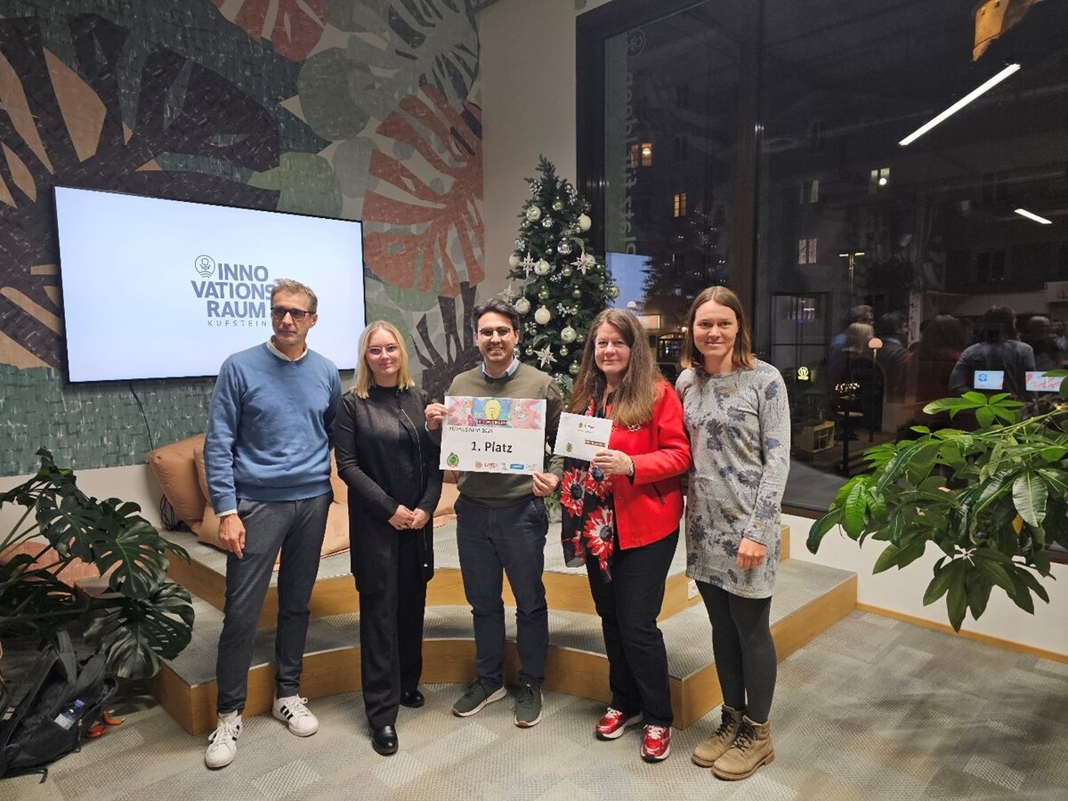 Eine Gruppe Menschen steht auf einem kleinen Podest, die Person in der Mitte hält ein Schild.