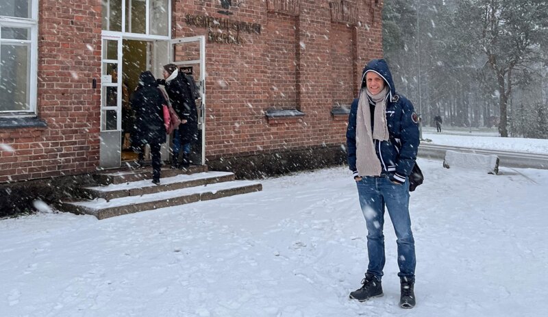 Mann steht vor Haus, Schnee fällt.