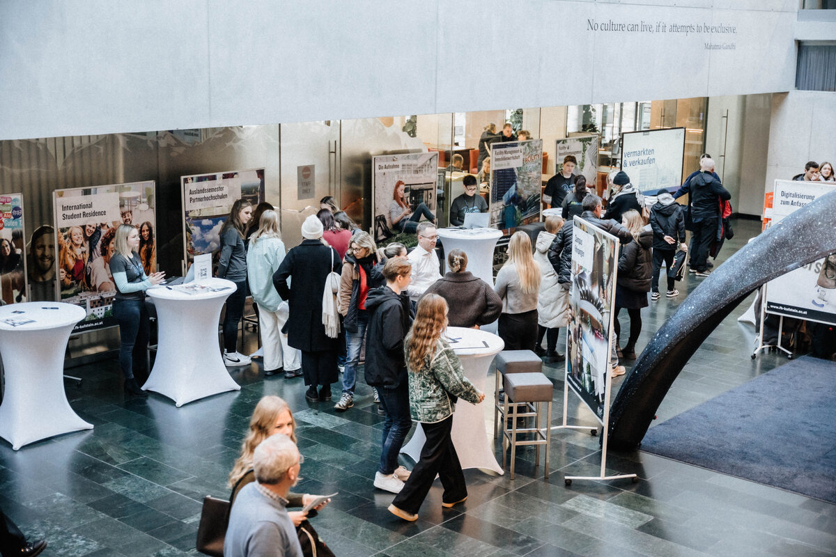 Blick von oben auf die Aula während eines Open House an der FH Kufstein Tirol mit Infoständen und Besucher:innen.
