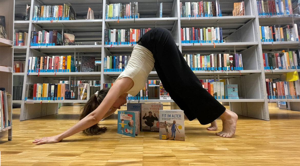 Studierende im herabschauenden Hund mit aufgeklappten Büchern unter ihr.