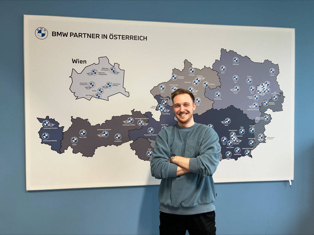 Junger Mann steht vor einer Karte mit BMW Logo.