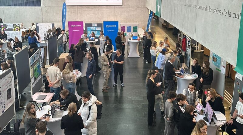 Blick von oben auf die Aula, wo mehrere Besucher:innen und Stände der Expo 2025 der FH Kufstein Tirol zu sehen sind. 
