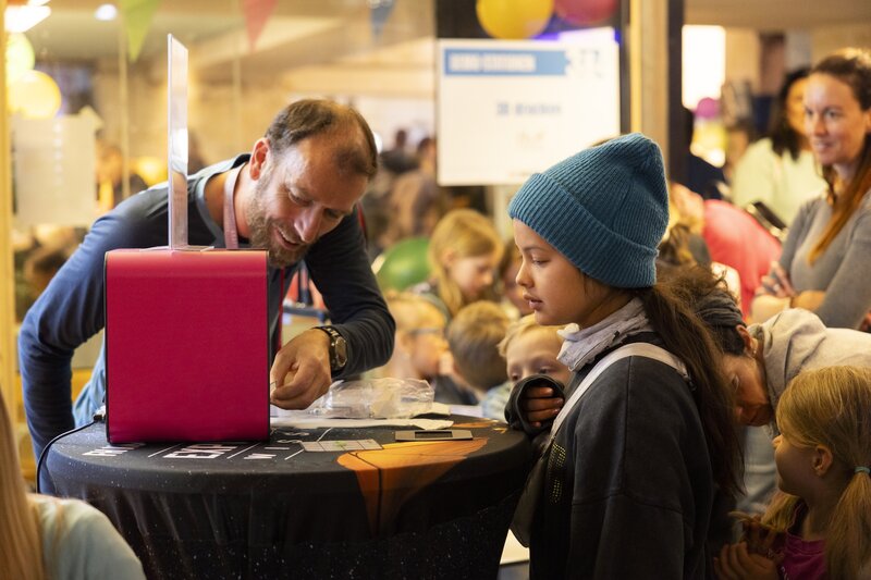 Markus drück auf den 3D-Drucker und ein Mädchen schaut zu