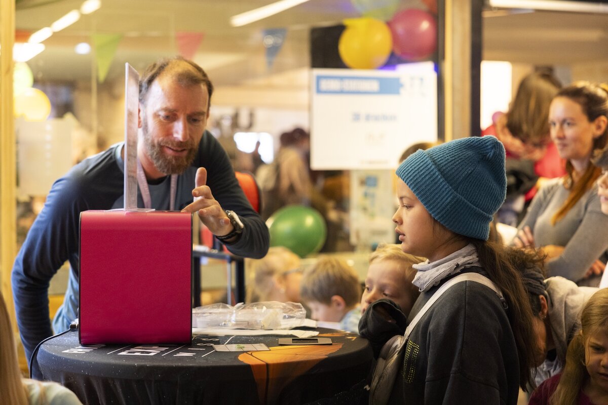 Markus drück auf den 3D-Drucker und ein Mädchen schaut zu