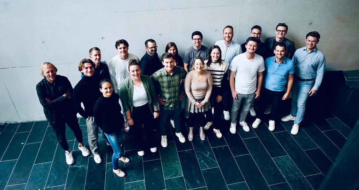 Praxisprojektgruppe mit Praxisprojektcoach vor grauen Wand