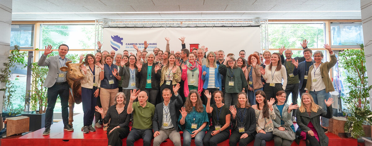 Viele Menschen sitzen auf einer Bühne und schauen direkt in die Kamera.