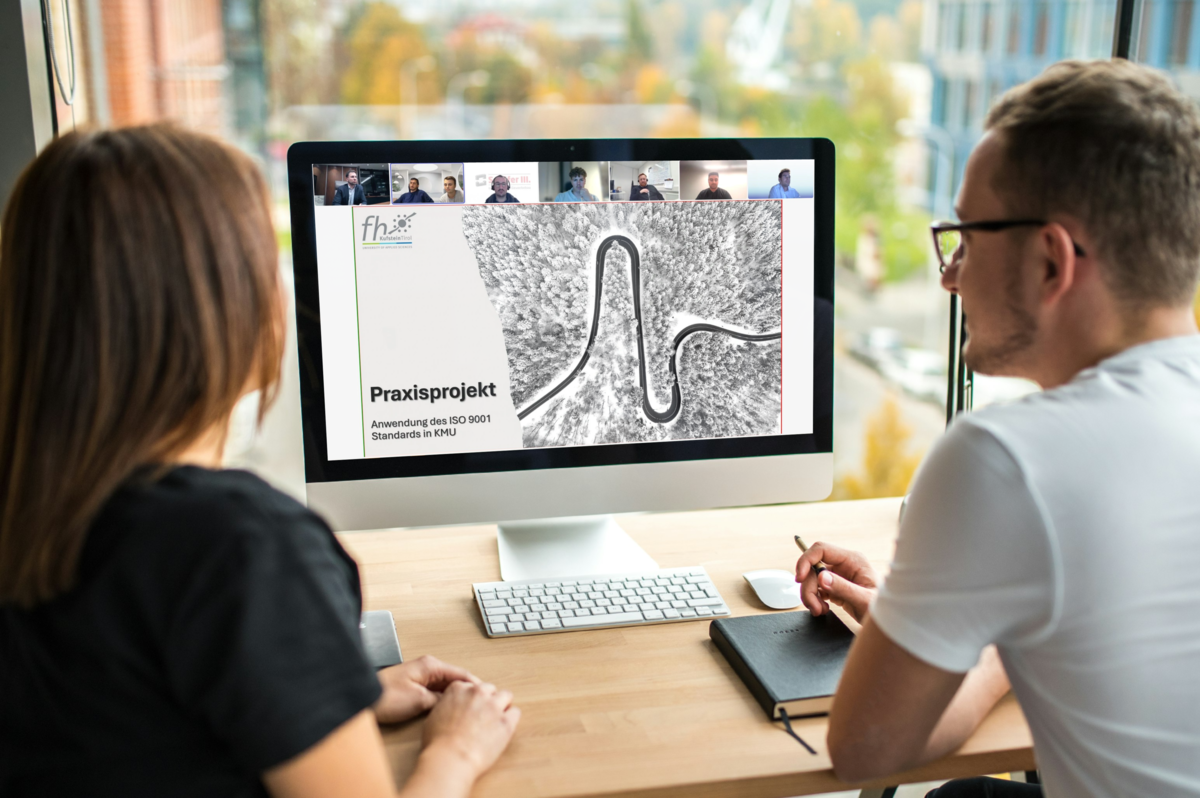 Zwei Personen sitzen vor einem Bildschirm, auf dem eine Präsentation zu sehen ist