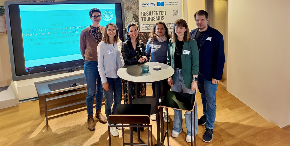 Personen stehen vor einem Roll-up und einem Bildschirm im Vortragsraum