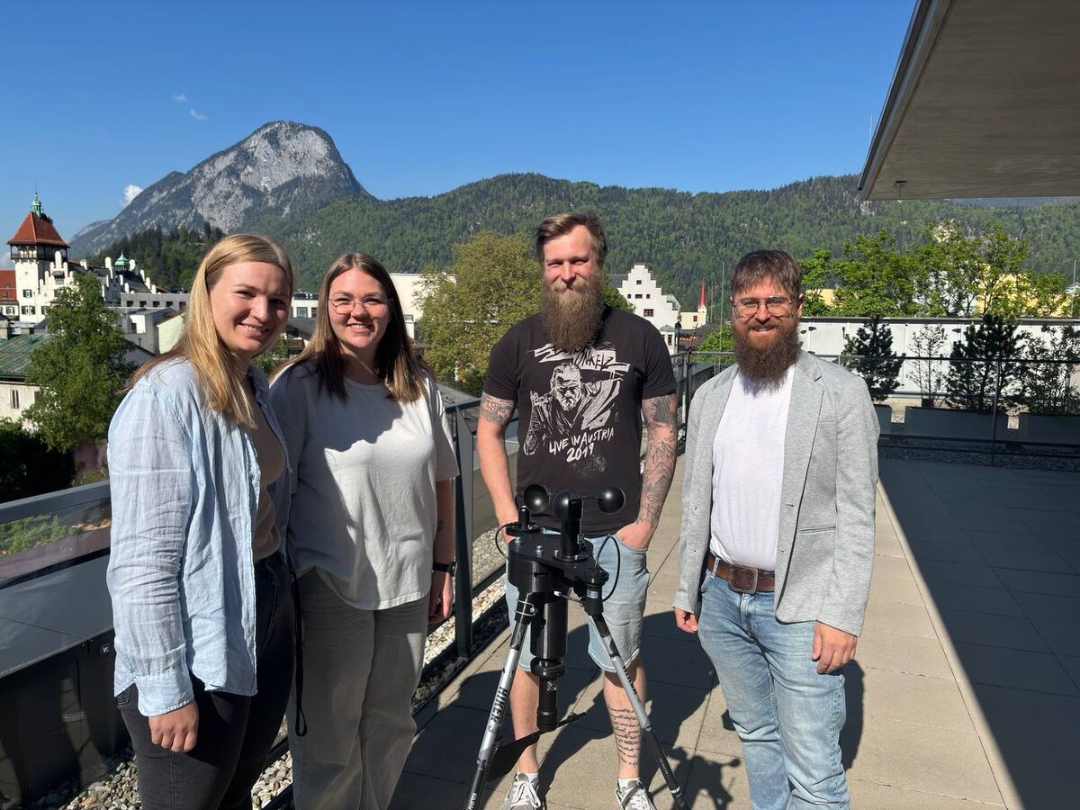 Gruppenbild mit 4 Personen und einem Aufnahmegerät in der Mitte.