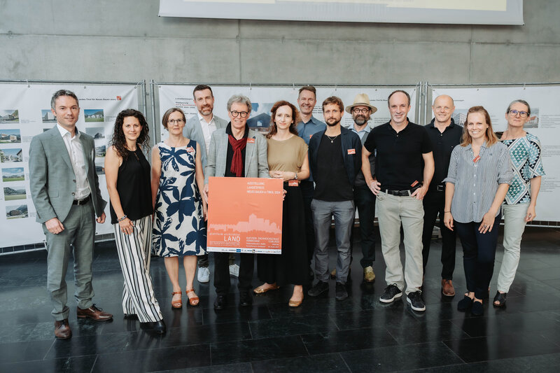 Eine Gruppe von Menschen steht Innen vor einem Bauzaunbanner.